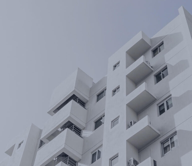 A modern white apartment building with geometric balconies and windows against a pale sky. Shadows create subtle contrast on the facade.