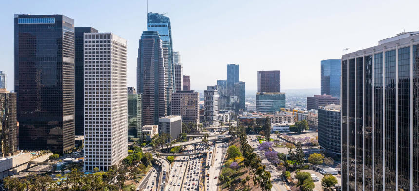 A panoramic view of a modern city skyline with towering skyscrapers and busy streets under a clear sky.