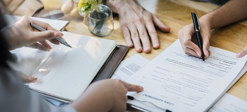 Hands engaged in note-taking and filling out forms on a wooden table.