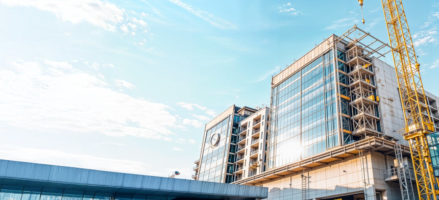 Modern building under construction, featuring large glass windows and a yellow crane against a clear blue sky.