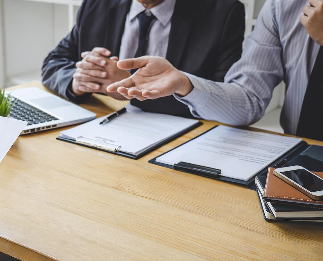 Two business professionals in suits discussing over documents and a laptop on a wooden table, engaged in a serious conversation.