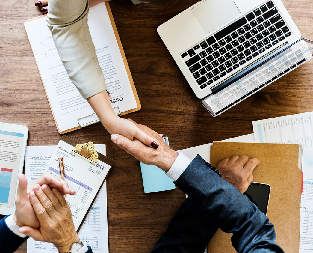 Two business professionals shake hands over a wooden table.