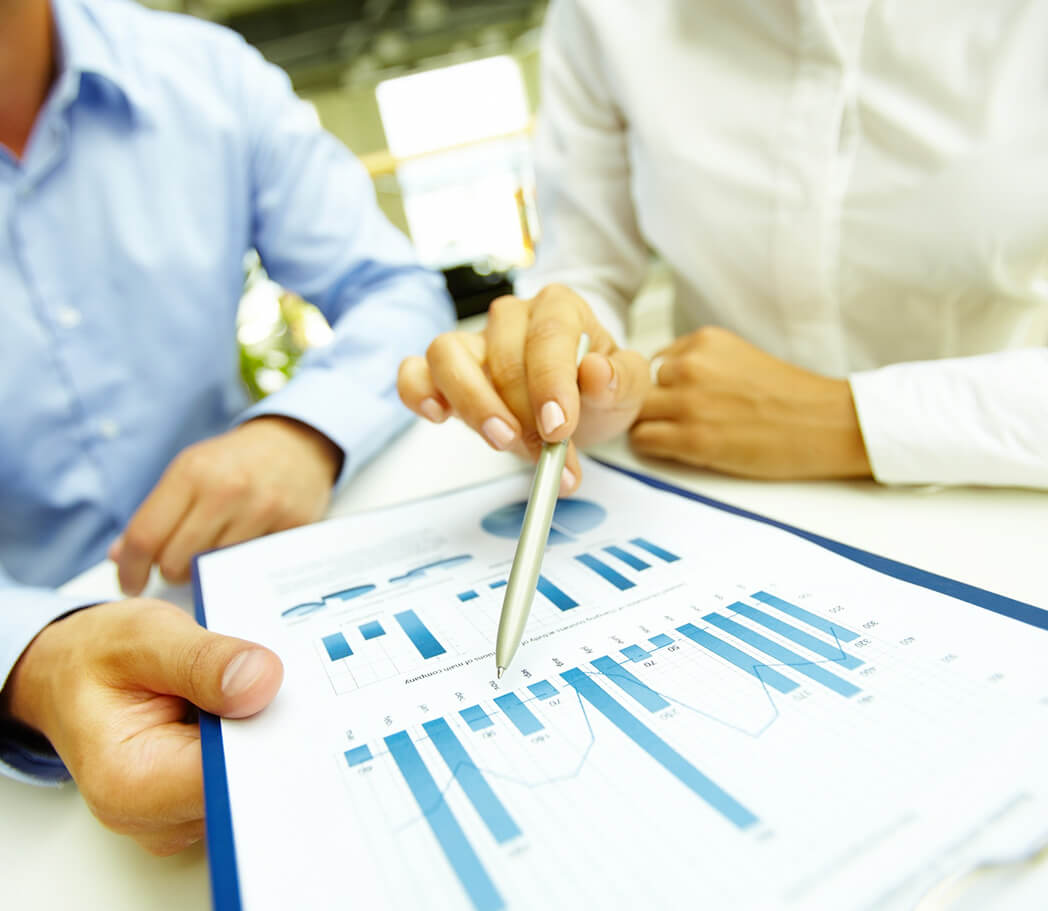 Two professionals discuss a report featuring graphs and charts, with one pointing at data on a document using a pen.