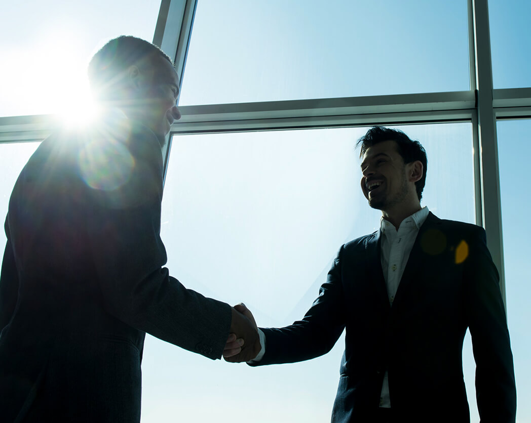 Two professionals shake hands, illuminated by sunlight streaming through large windows, symbolizing partnership or agreement.