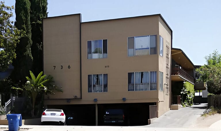 A two-story apartment building with a car parked in front, showcasing a residential neighborhood setting.