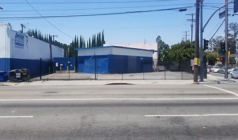 A blue building with a fence and several cars parked in front, set against a clear sky.