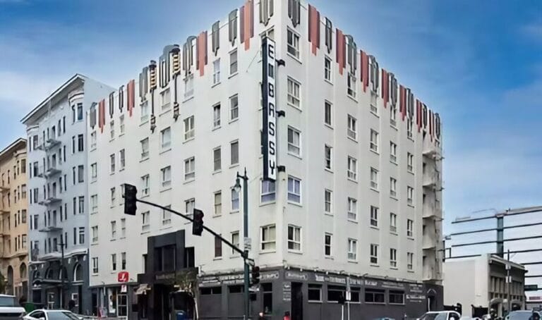 A five-story building with a modern facade, stands at a busy street corner under a clear blue sky.