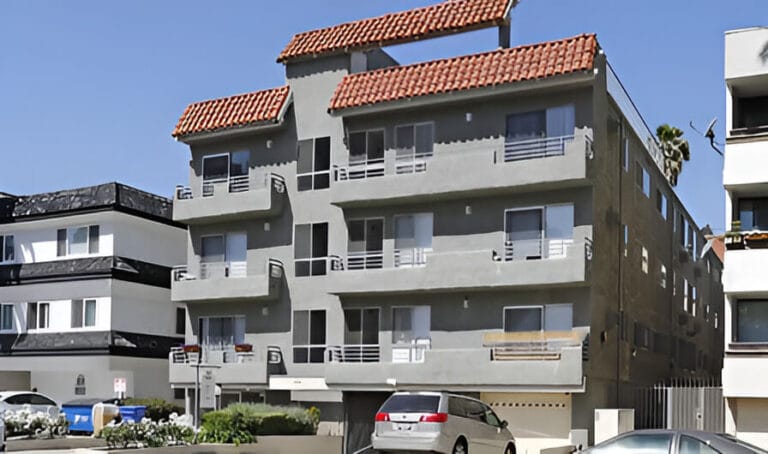 A grey apartment building with several cars parked in front, showcasing a typical urban residential setting.