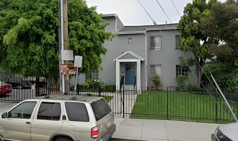 A house with a fence and a parked car in front, showcasing a suburban residential setting.