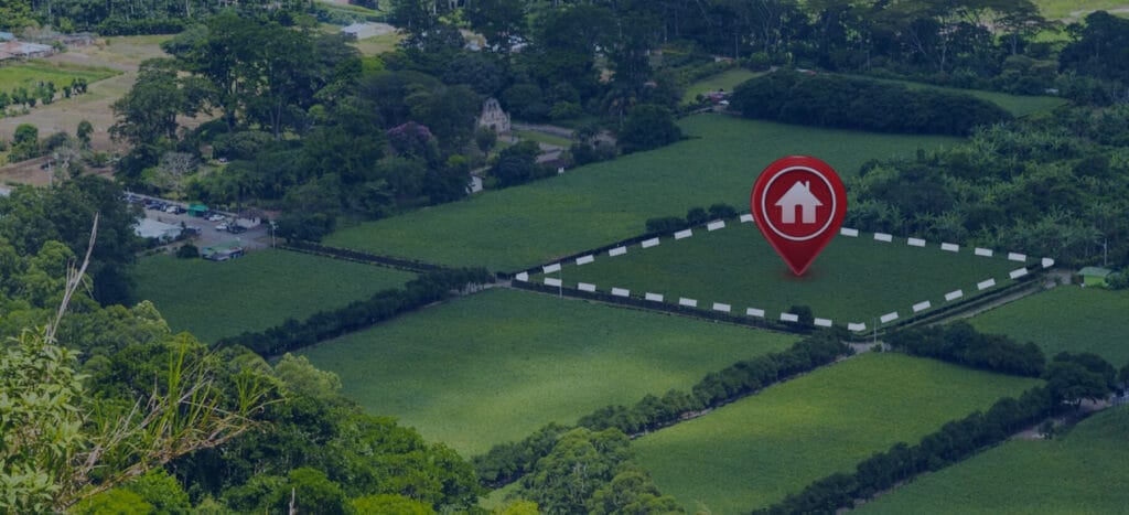 A red pin marks a location on a green field surrounded by trees and houses in the background.