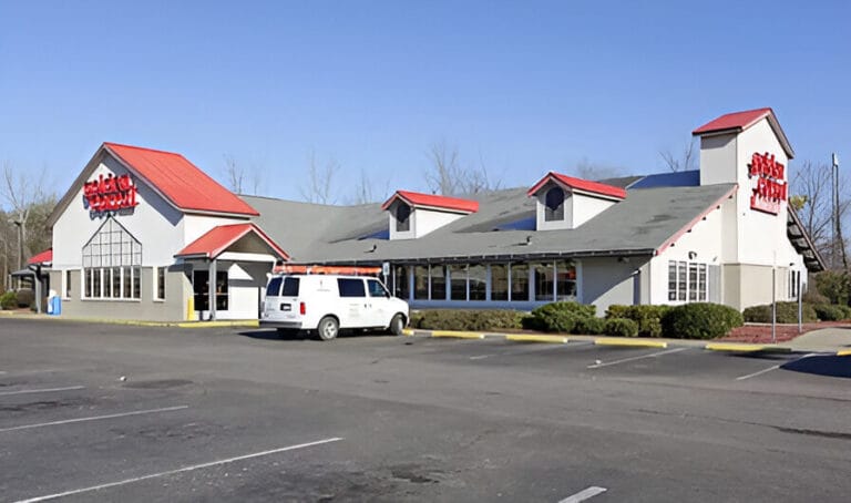 A retail property with a red roof, surrounded by several white cars parked in the lot.