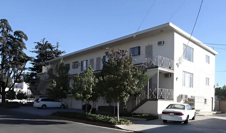 A white apartment building with a car parked in front, showcasing a modern urban living environment.