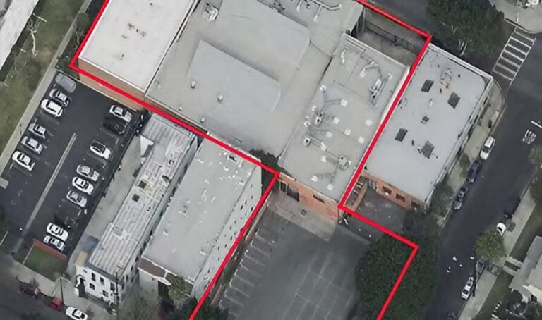 Aerial view of a commercial building complex marked in red, with adjacent parking lot and surrounding streets visible.