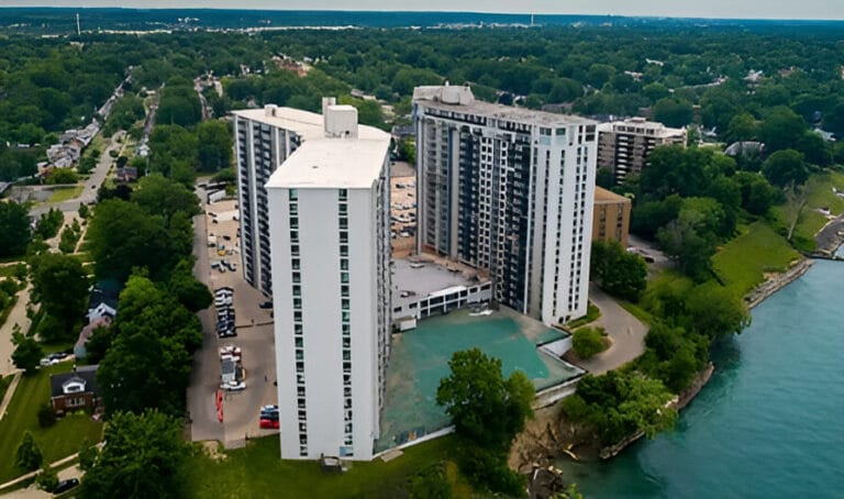 Aerial view of a large apartment building situated alongside a river, showcasing the surrounding landscape and waterway.