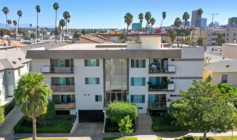 Aerial view of an apartment complex surrounded by lush palm trees, showcasing the layout and greenery of the area.