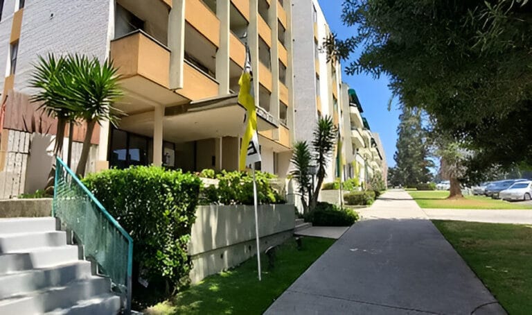 An apartment building situated alongside a street, showcasing its exterior and surrounding environment.