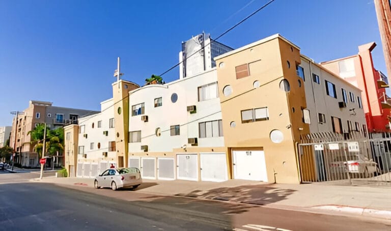 An apartment building stands at the corner of a street, showcasing its modern architecture and surrounding urban landscape.