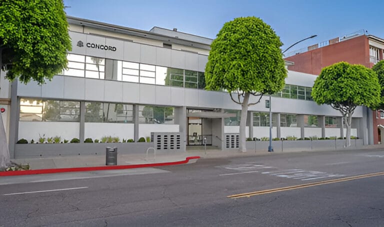 An office building stands at the corner of a street, showcasing its modern architecture and urban surroundings.