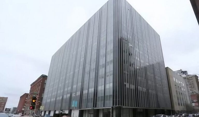 Modern glass building with vertical stripes, set against a cloudy sky, adjacent to older brick structures and traffic signals.