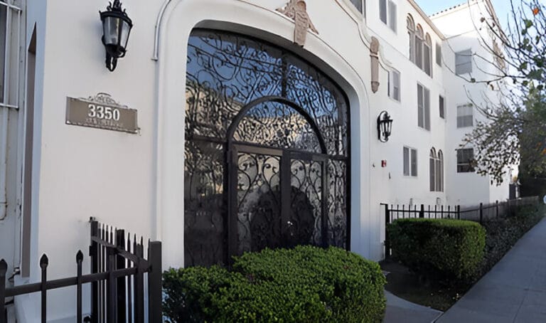 The entrance of a building featuring an ornate wrought iron gate, framed by stone walls and greenery.