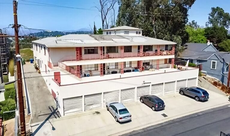 Two-story apartment building with a parking lot filled with cars in front.